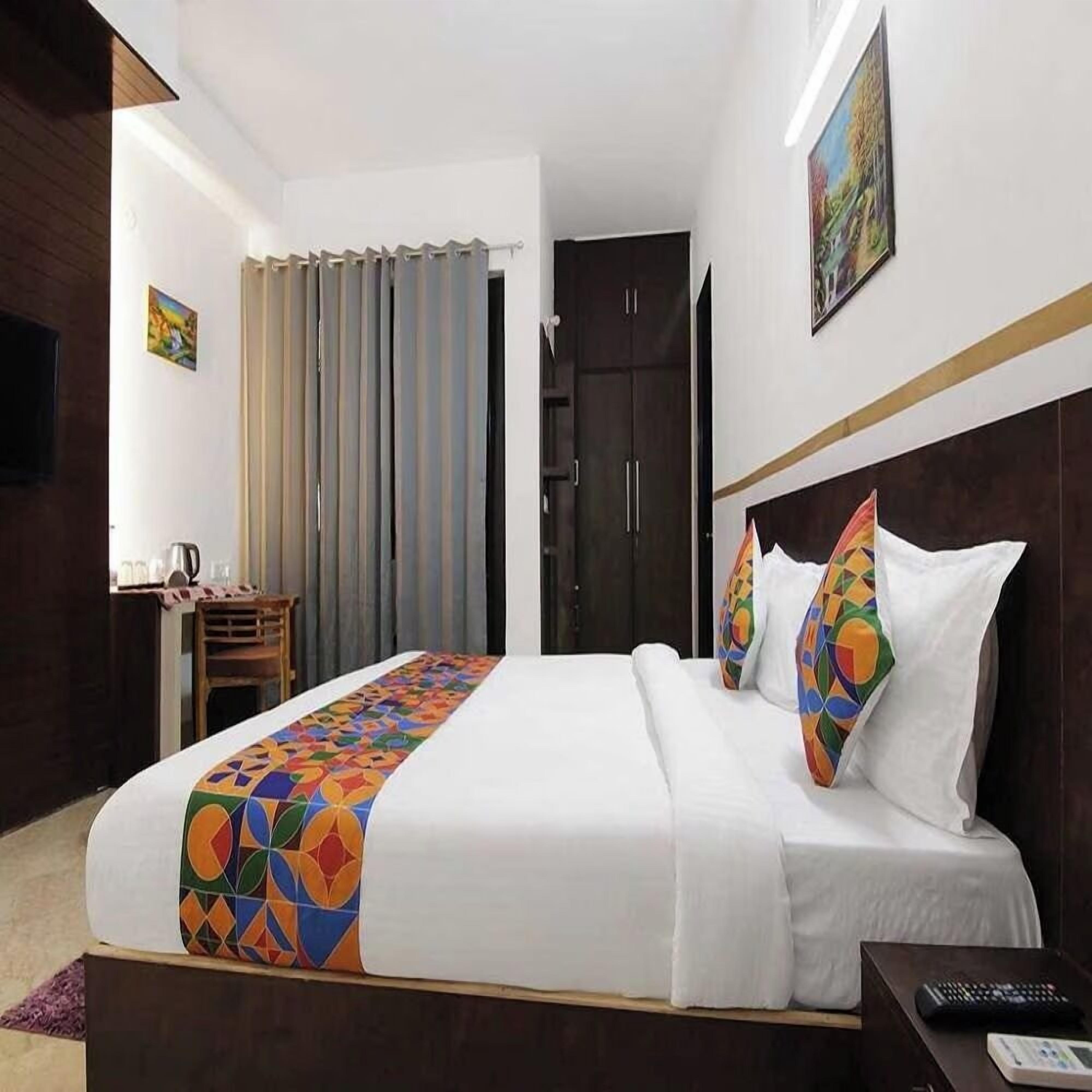A hotel room with a bed, a desk, a chair, a TV, and a painting on the wall.