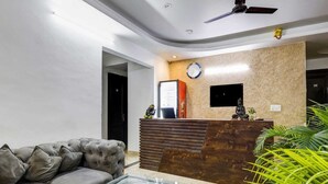 A modern reception area with a sofa, a reception desk, a clock, and a ceiling fan. - Hotel Viraj (Gurugram)