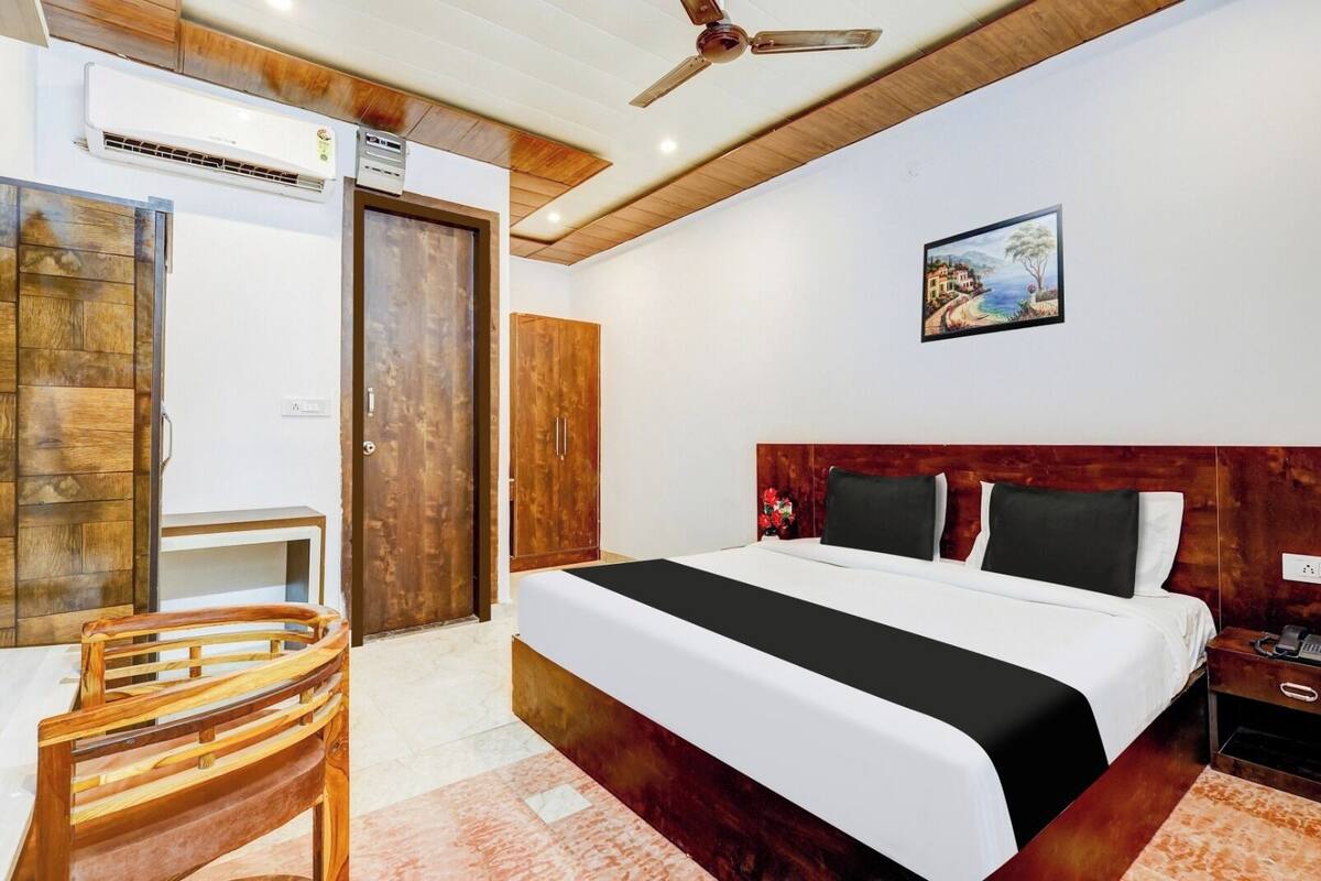 A bedroom with a wooden headboard, a bed with white bedding, a wooden chair, a desk, and a ceiling fan.
