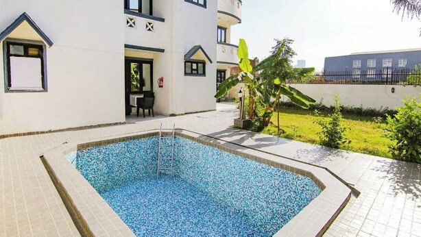A swimming pool with a tiled deck, a small outdoor seating area, and a building with balconies and windows. - Hotel Viraj (Gurugram)