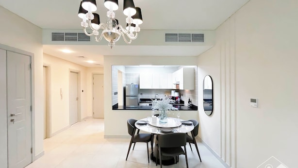Een moderne keuken met witte kasten, een zwart aanrecht en een eethoek met een ronde tafel en stoelen.