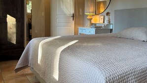 A bedroom with a large bed, a bedside table, a mirror, and a door leading to another room.