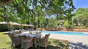 A pool area with lounge chairs and umbrellas, surrounded by greenery and a stone staircase.