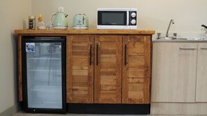Une cuisine compacte équipée d’un réfrigérateur, d’un four à micro-ondes et d’une bouilloire, le tout posé sur un plan de travail en bois.