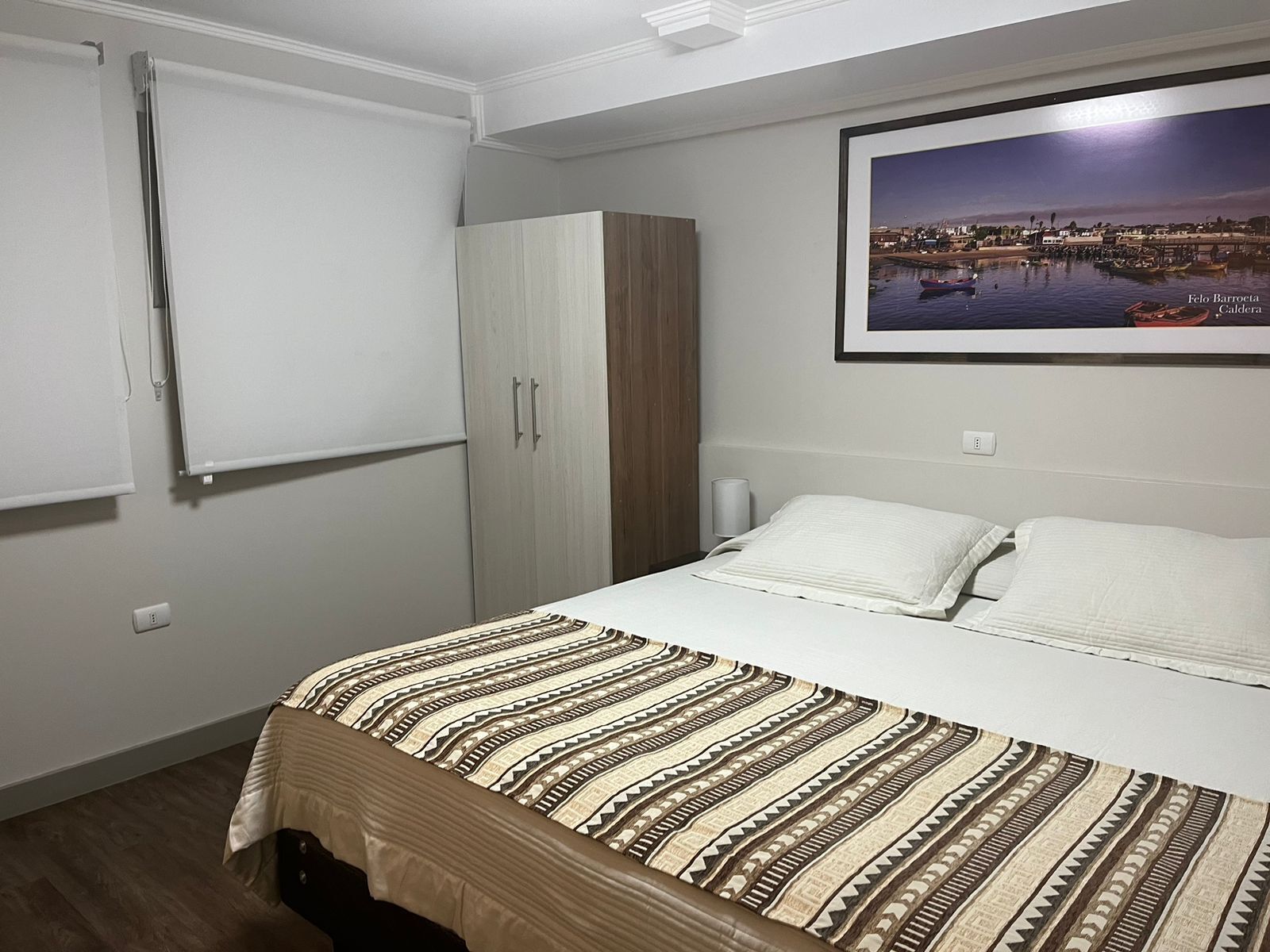 A bedroom with a bed, a wardrobe, a nightstand, and a framed picture on the wall.