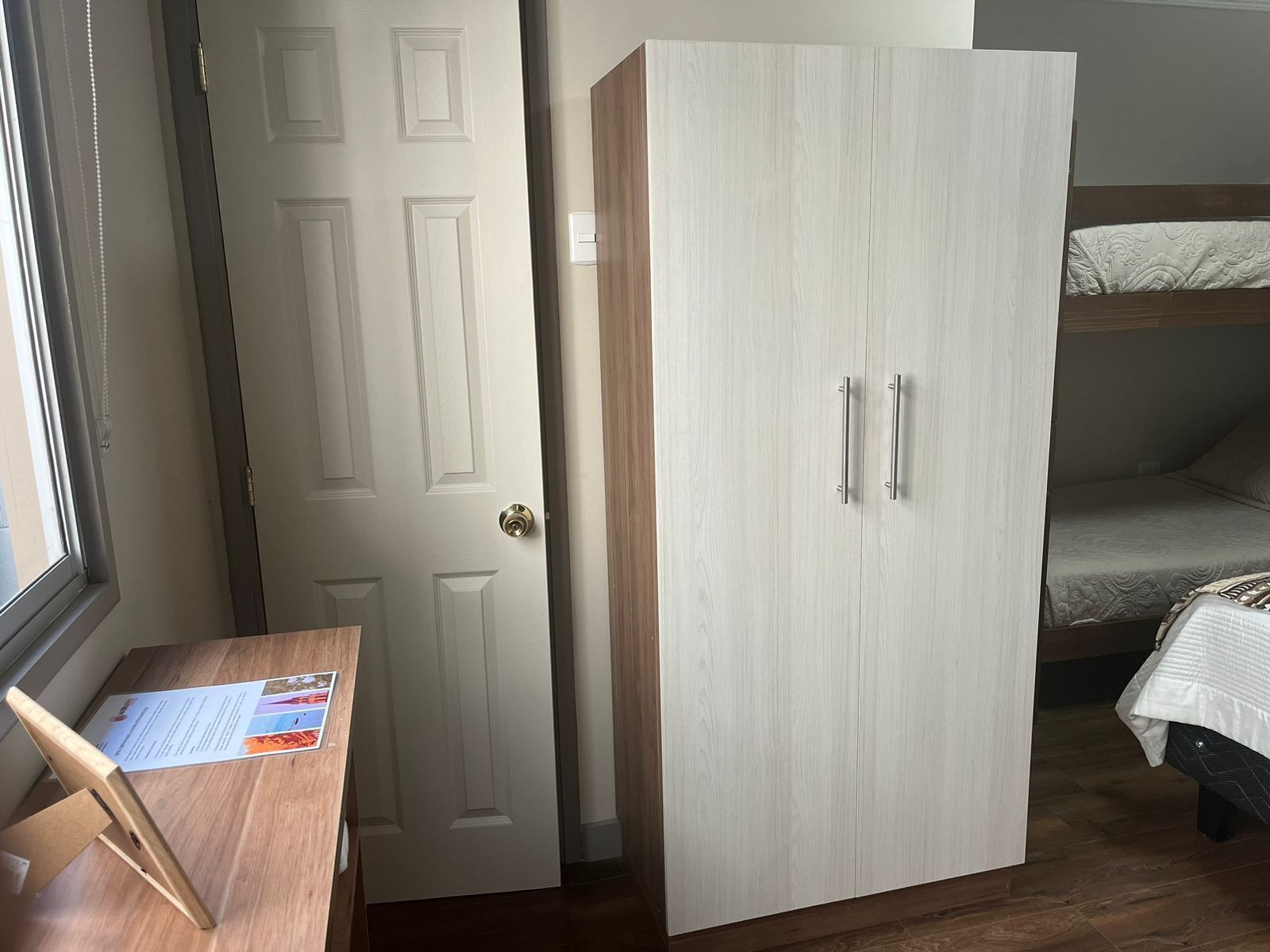 A bedroom with a bed, a wooden desk, and a wardrobe.
