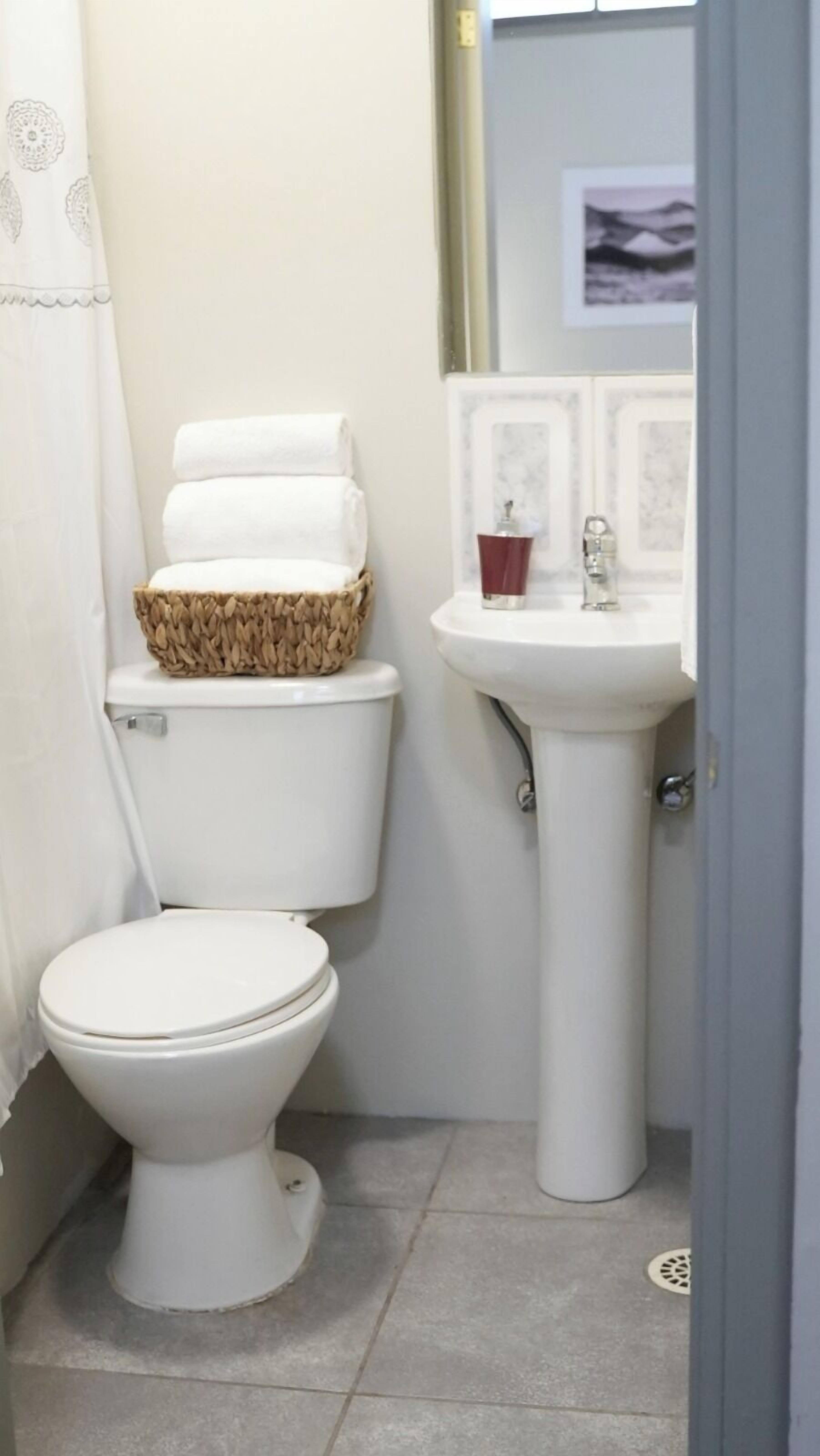 A small, clean bathroom with a white toilet, a white sink, and a decorative basket on the toilet tank.