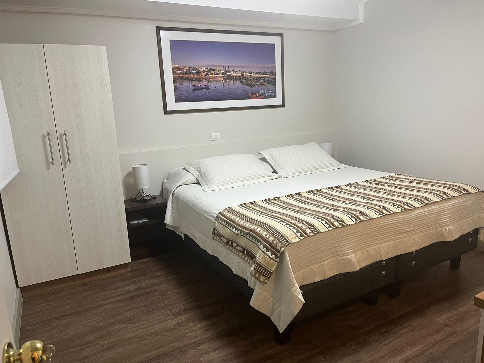 Un dormitorio con cama, mesita de noche, armario y un cuadro en la pared.