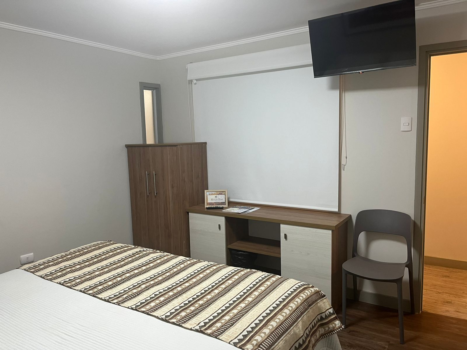 Un dormitorio con cama, escritorio con silla, armario y televisor montado en la pared.