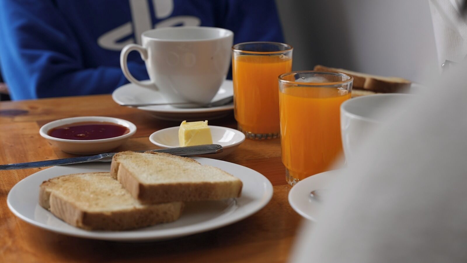 A breakfast setting with toast, butter, jam, and orange juice on a wooden table.