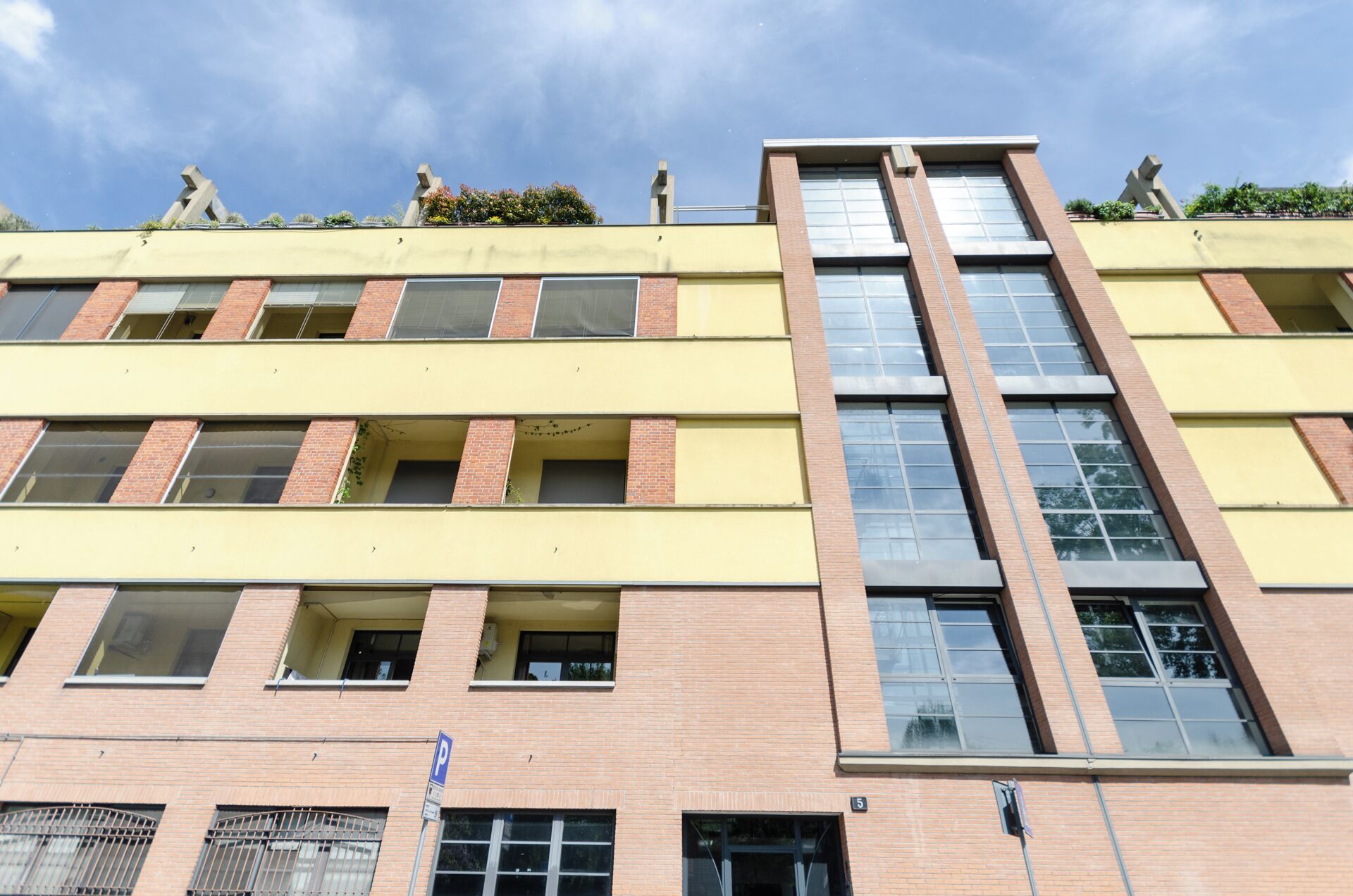 A multi-story building with a yellow facade, large windows, and a prominent central glass section.