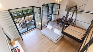 A modern loft bedroom with a large window, a sofa bed, a dining area, and a staircase. - VivimiHome-Esclusivo loft con terrazzo (Milan)