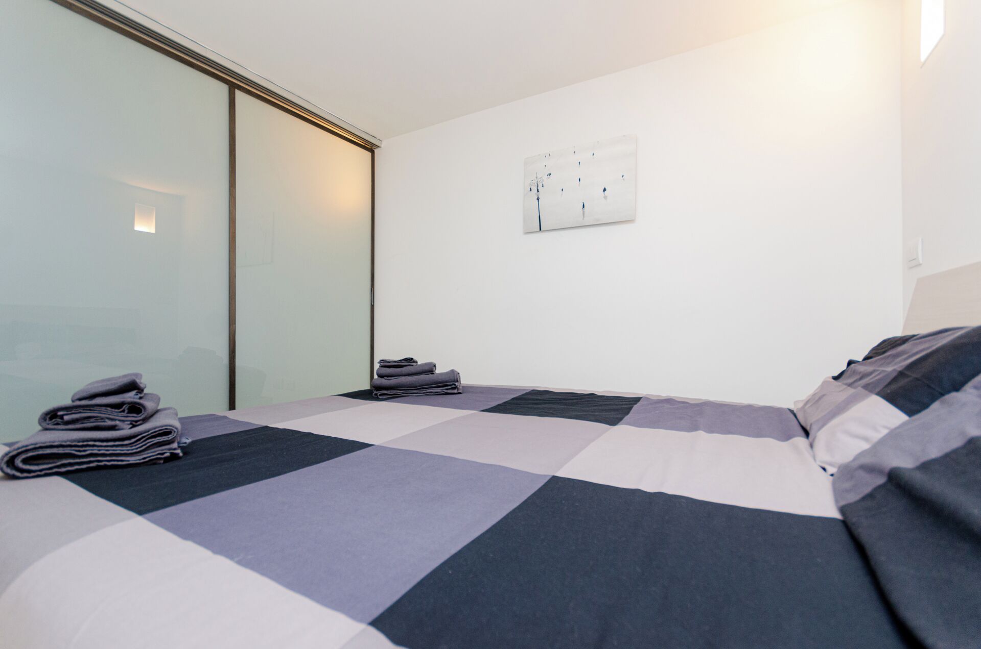 A modern hotel room with a large bed, a glass partition, and a wall-mounted light switch.