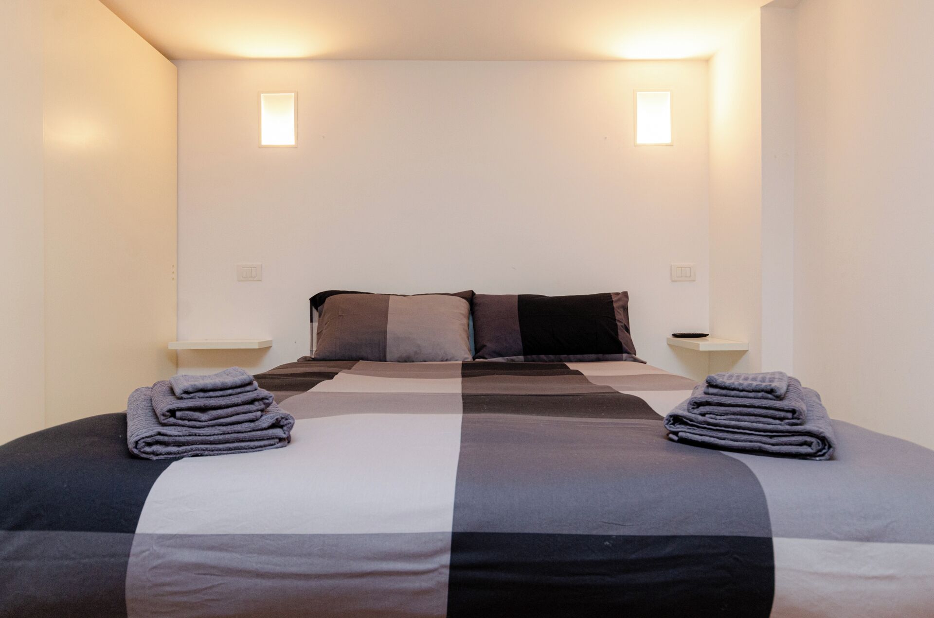 Una habitación de hotel con una cama, dos mesitas de noche y dos lámparas de pared.