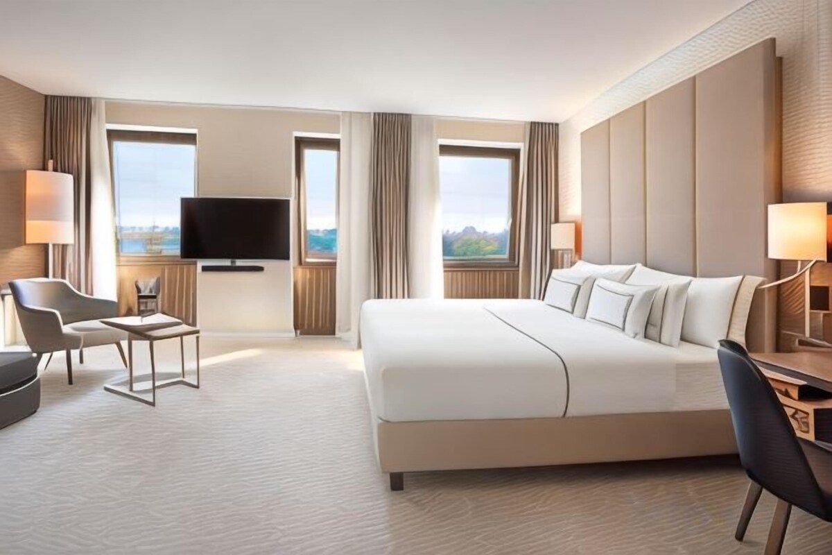 Habitación de hotel con una cama grande, un escritorio, una silla, un televisor y vistas a la ciudad.