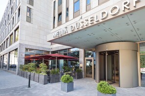 Entrada de hotel con diseño moderno, que incluye un gran letrero, asientos al aire libre y plantas en macetas.