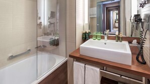 Ein modernes Badezimmer mit einer in Glas eingefassten Dusche, einem weißen Waschbecken mit Holzablage und einem an der Wand befestigten Föhn.