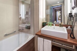 A modern bathroom with a glass-enclosed shower, a white sink with a wooden countertop, and a hairdryer on the wall. - Meliá Düsseldorf (Düsseldorf)