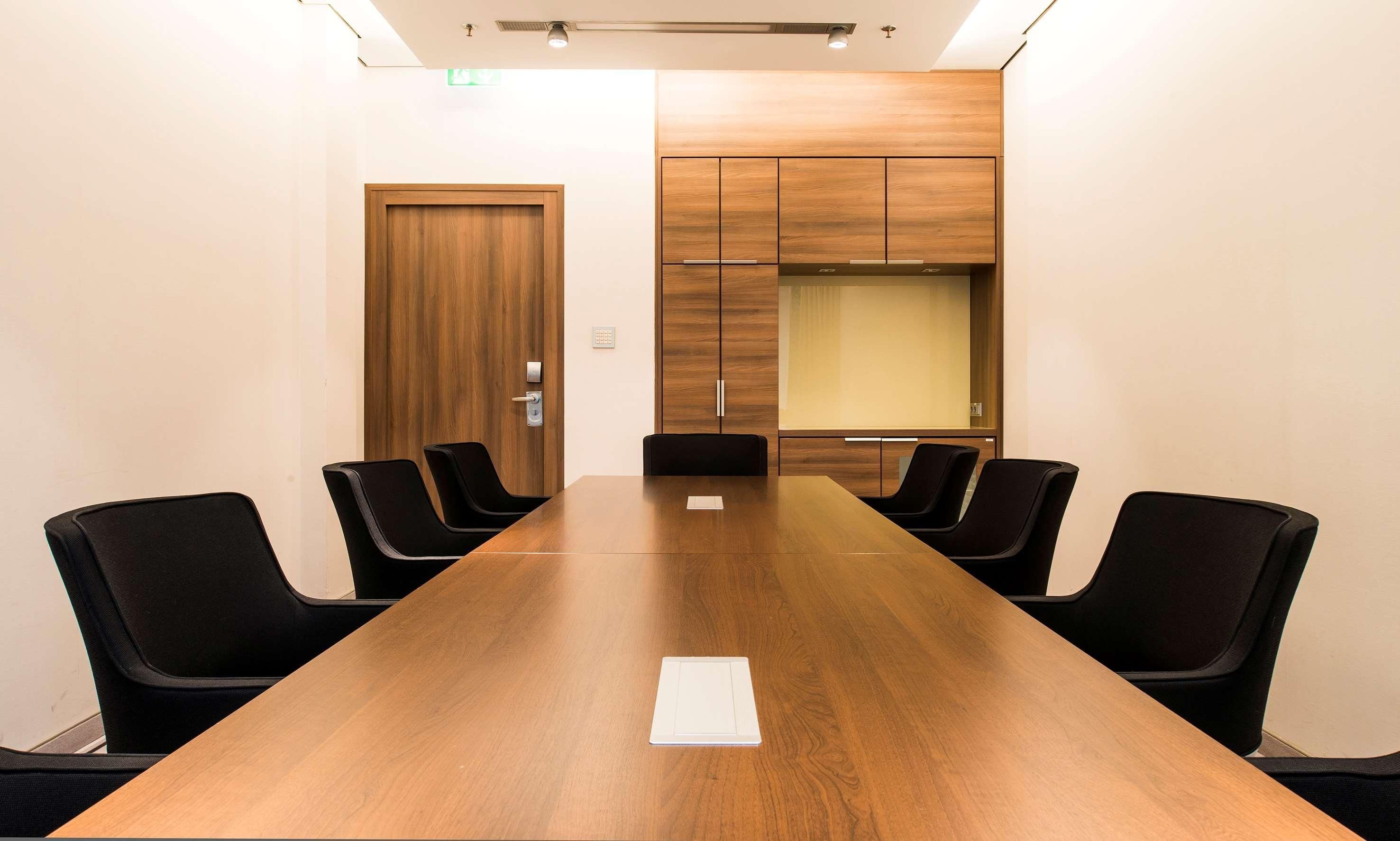 A conference room with a long wooden table, black chairs, a wooden door, and a built-in cabinet with a glass partition.