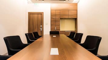 Un salón de conferencias con una larga mesa de madera, sillas negras, una puerta de madera y un armario empotrado con una partición de vidrio.