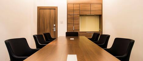 A conference room with a long wooden table, black chairs, a wooden door, and a built-in cabinet with a glass partition.