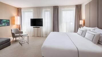 Habitación de hotel con una cama grande, una televisión de pantalla plana, una silla, una mesita y televisión en la pared.