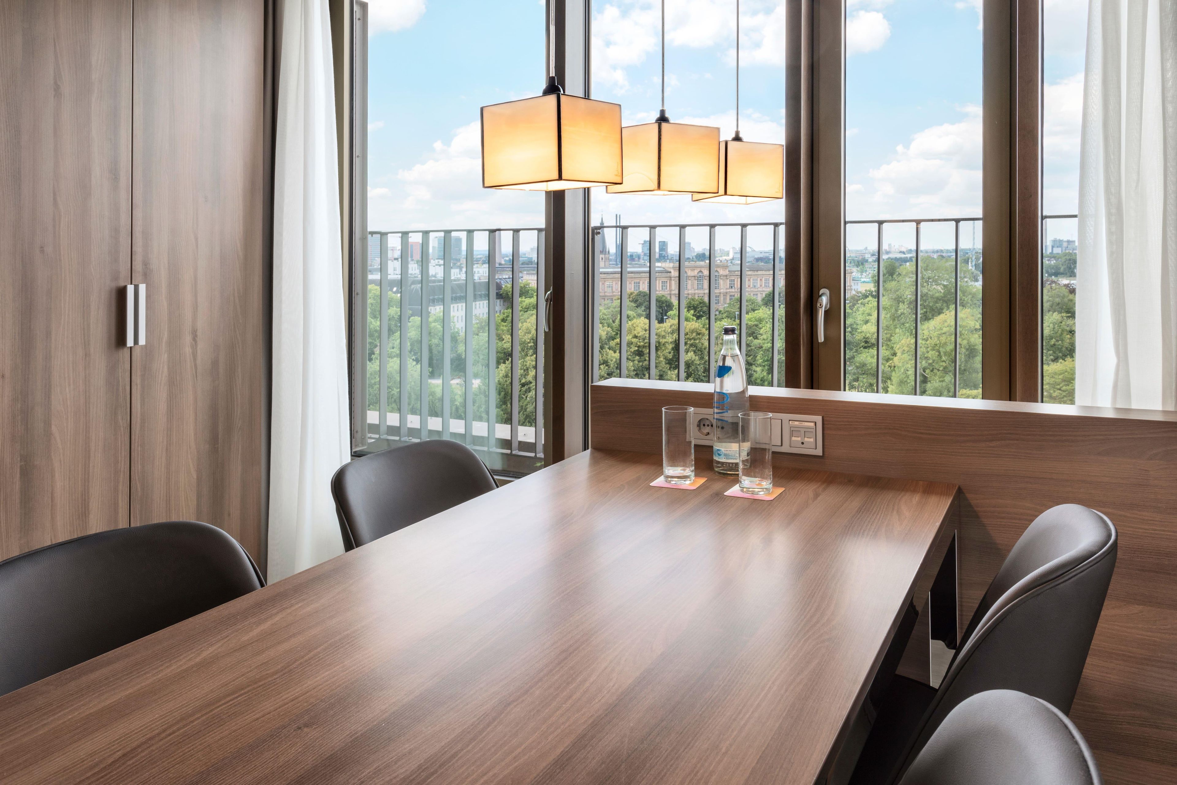 Sala de conferências com mesa de madeira, cadeiras pretas e vista para o verde através de amplas janelas.