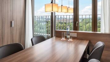 Sala de conferências com mesa de madeira, cadeiras pretas e vista para o verde através de amplas janelas.
