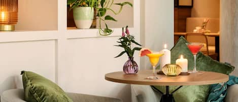 A cozy seating area with a round table, green cushions, a vase with flowers, and a candle.