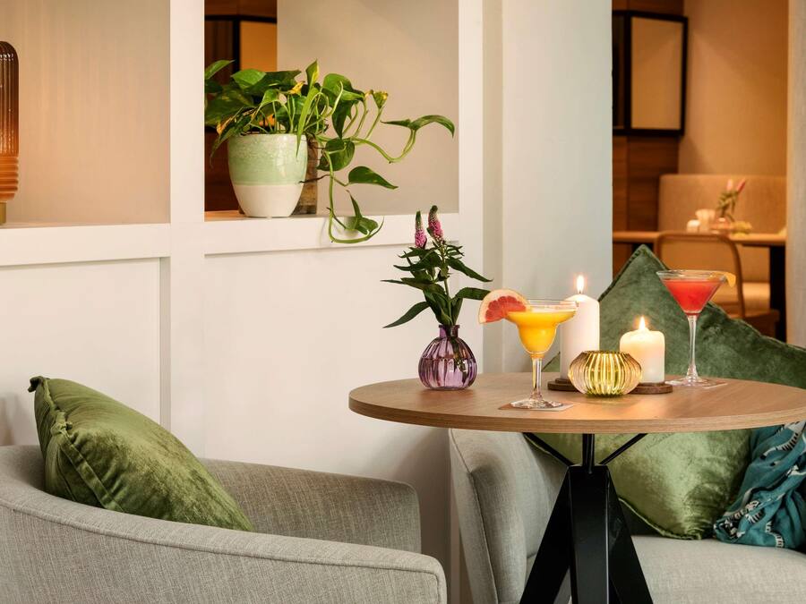Un rincón acogedor con una mesa redonda, cojines verdes, un jarrón con flores y una vela.