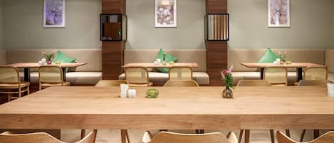 A modern dining area with a long wooden table, cushioned seating, and pendant lighting.