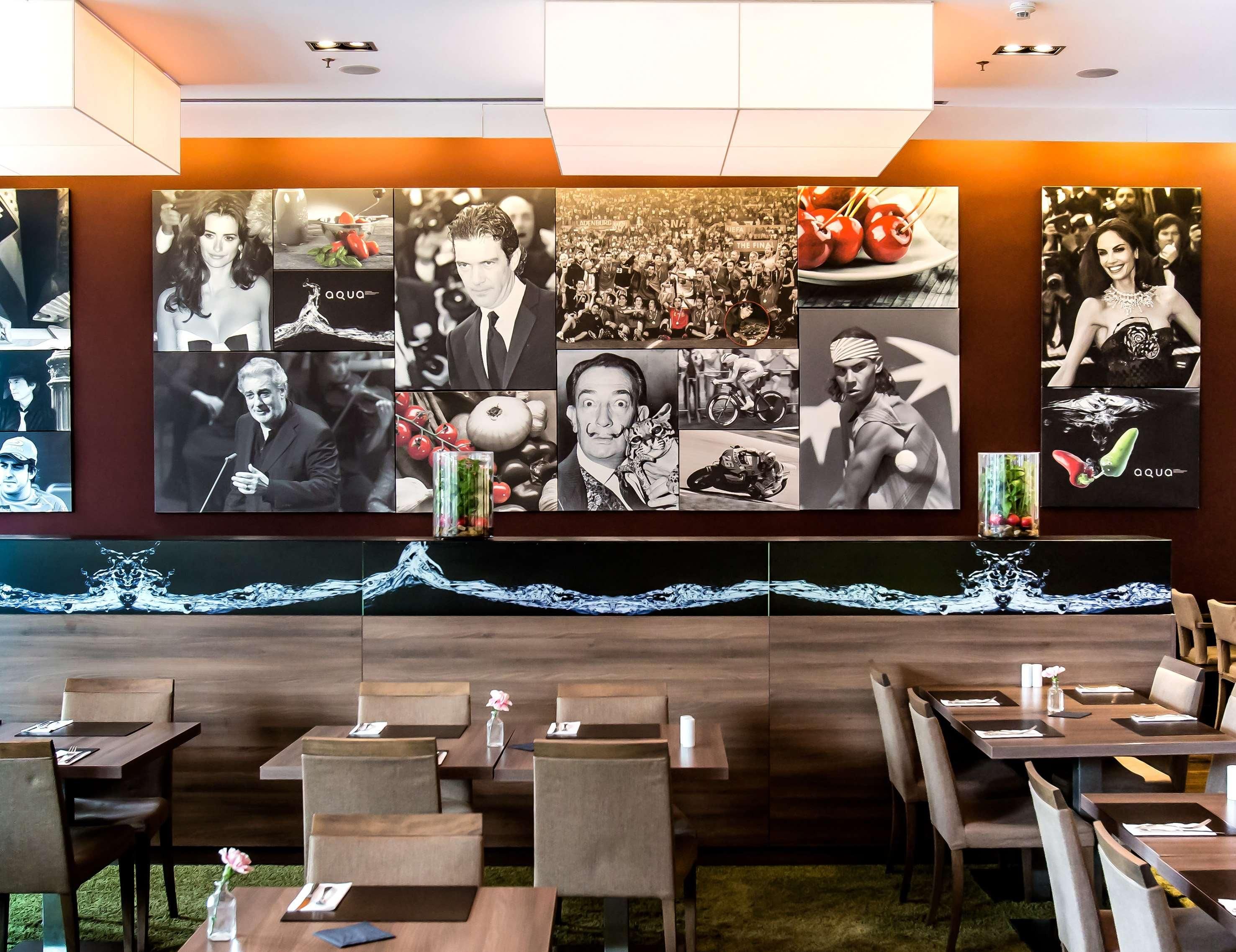 L’intérieur d’un restaurant est agrémenté d’un long mur recouvert de photographies, de tables et de chaises en bois.
