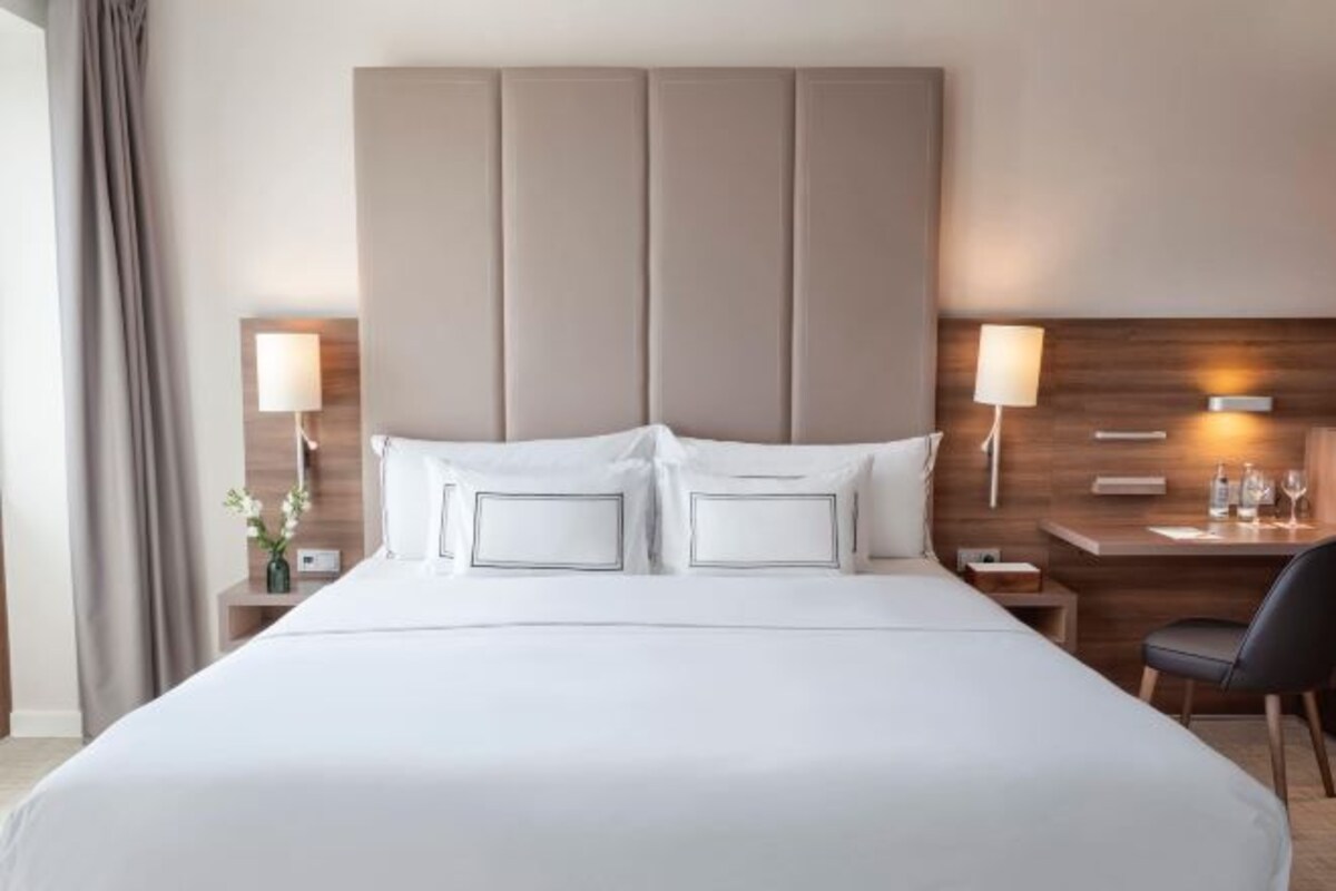 Une chambre d’hôtel avec un grand lit, deux tables de chevet, un bureau avec une chaise et une tête de lit en bois.
