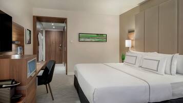 A hotel room with a bed, a desk with a coffee machine, a TV, and a painting on the wall.