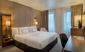 Una habitación de hotel con una cama grande, dos mesitas de noche con lámparas, un escritorio y una silla.