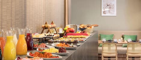 A buffet with various food items and beverages, a sofa, and two chairs in a modern room.