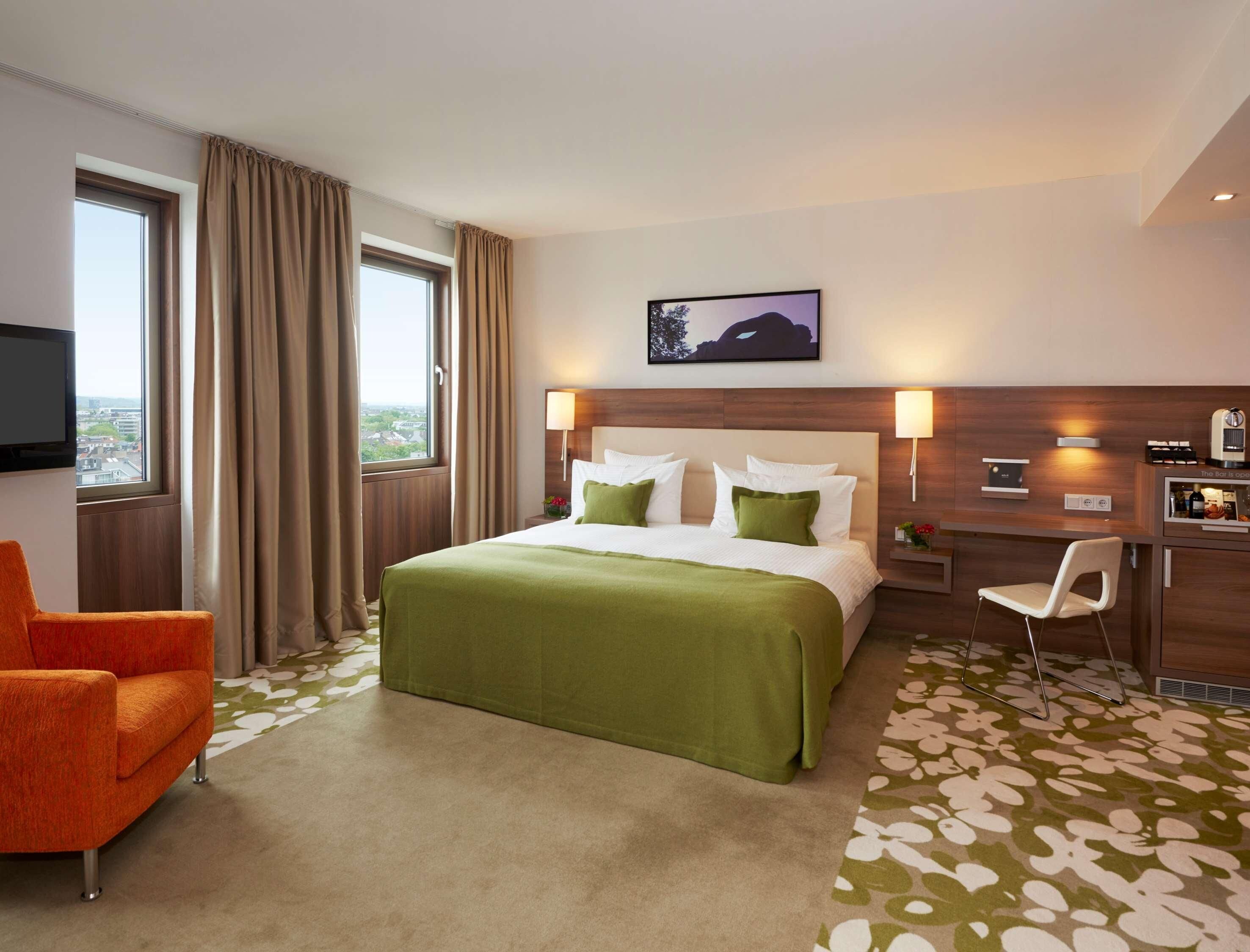 Een hotelkamer met een groot bed, een televisie aan de muur, een bureau met een stoel en uitzicht op de stad door het raam.