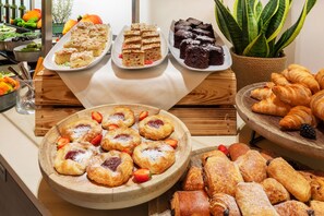 A buffet table with various pastries and desserts, including cakes, brownies, and croissants.