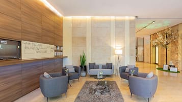 A modern lobby with grey sofas, a coffee table, a TV, and a sign encouraging exploration of the city.