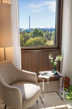 A room with a view of a park, a chair, a small table with a vase of flowers, and a lamp. - Meliá Düsseldorf (Düsseldorf)