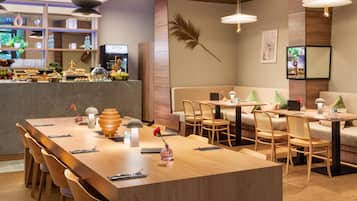 Un restaurante moderno con una larga mesa de madera, asientos acolchados e iluminación colgante.
