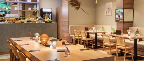 A modern restaurant with a long wooden table, cushioned seating, and pendant lighting.