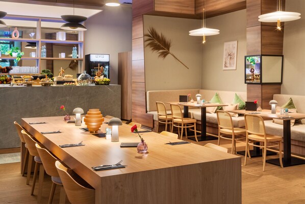 A modern restaurant with a long wooden table, cushioned seating, and pendant lighting. - Meliá Düsseldorf (Düsseldorf)