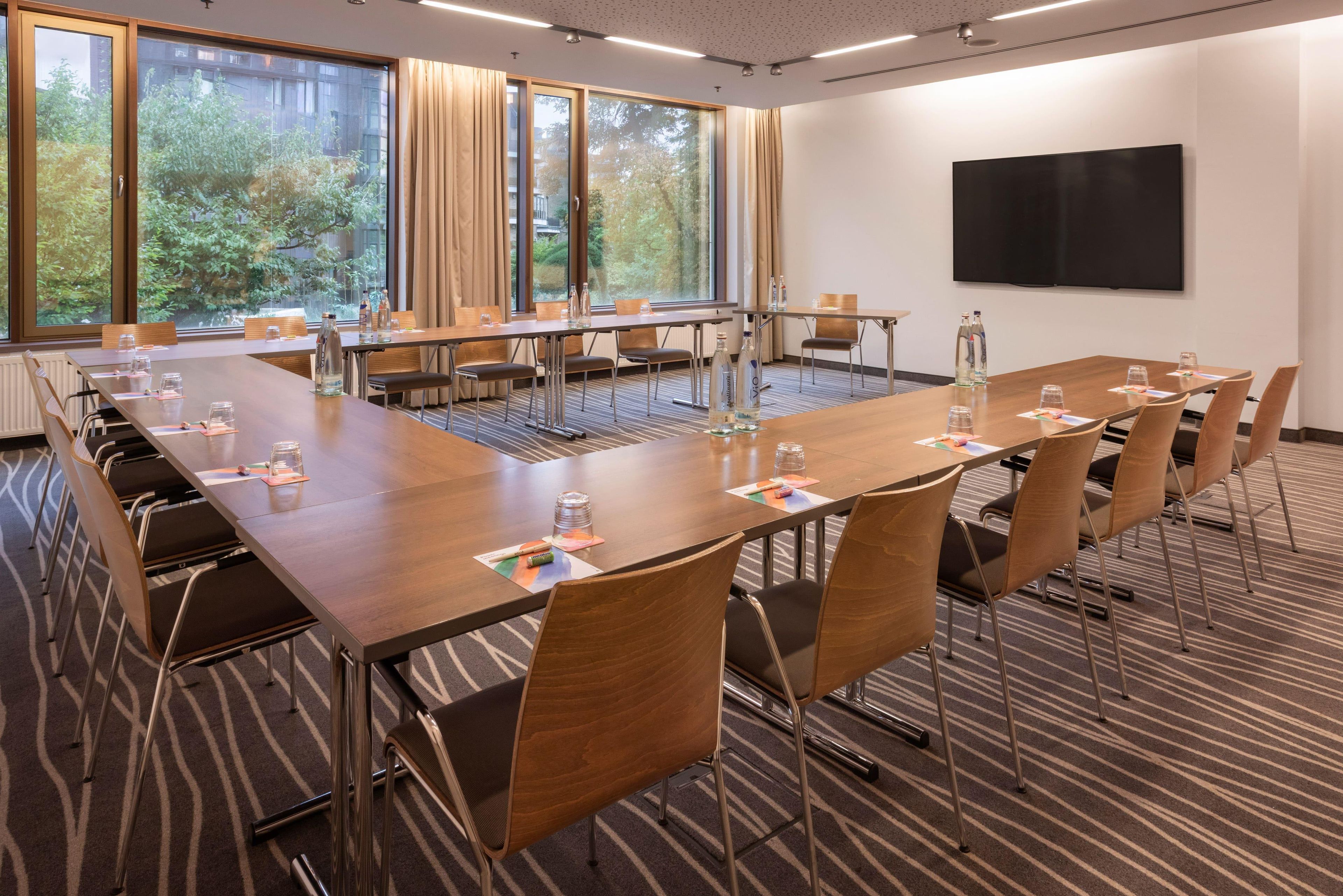 Ein Konferenzraum mit einem langen Tisch, Stühlen und einem großen Fenster mit Vorhängen.
