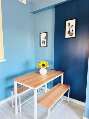 Quarto de canto com parede azul, mesa de madeira com um vaso de girassóis e duas fotos emolduradas.
