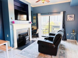 Een woonkamer met een open haard, een zwarte bank, een televisie aan de muur en uitzicht op de omgeving.