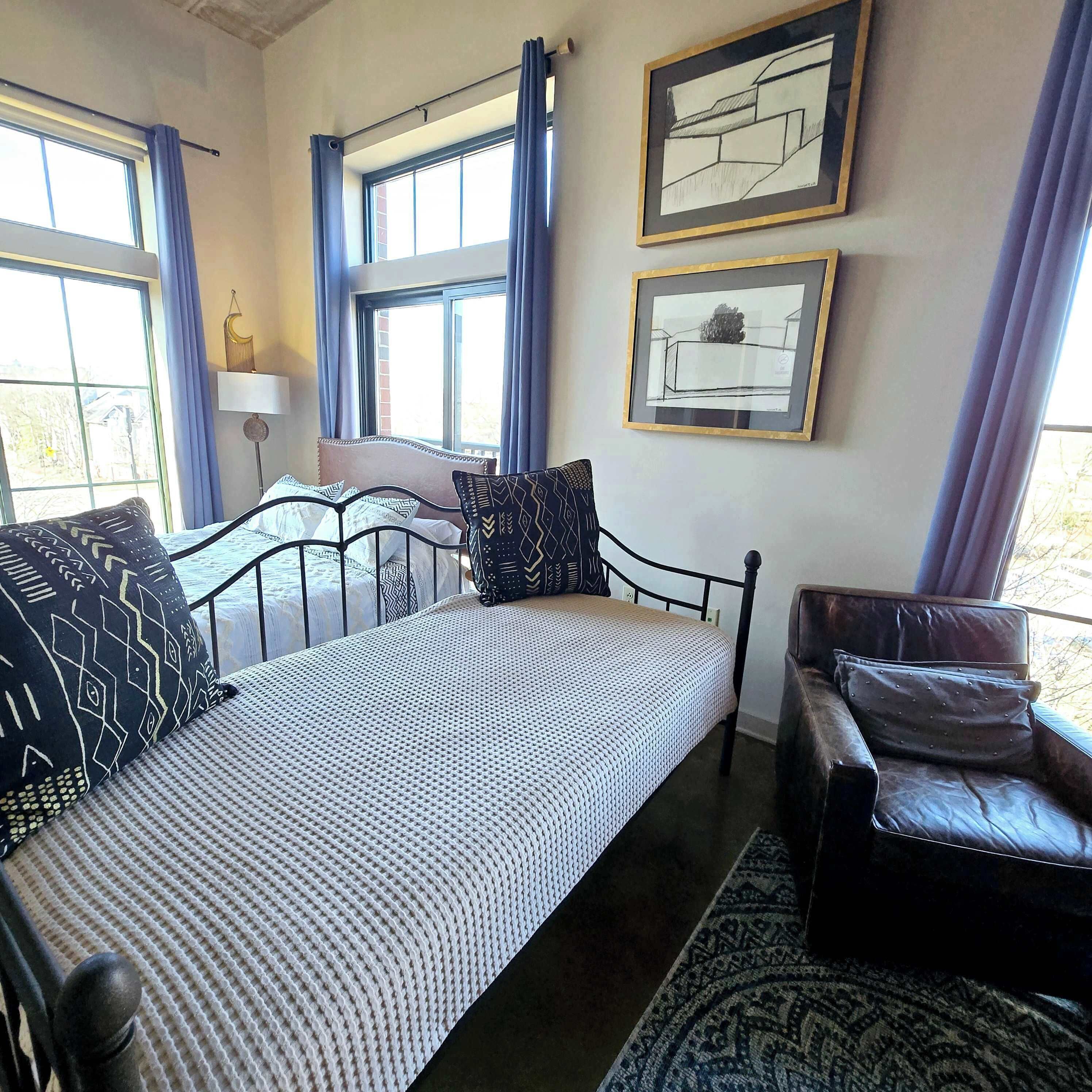 Quarto com uma cama, uma cadeira, uma janela e duas obras de arte emolduradas na parede.