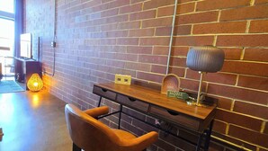 Een kamer met bakstenen muren, een bureau, stoel en een wandlamp.