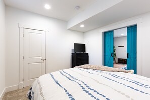 Een slaapkamer met een bed, een televisie op een standaard, een deur en een blauwe deur die naar een andere kamer leidt.