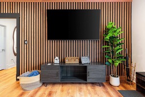 Un salon moderne avec un meuble TV en bois foncé, un téléviseur à écran plat, une plante en pot et un panier en osier.